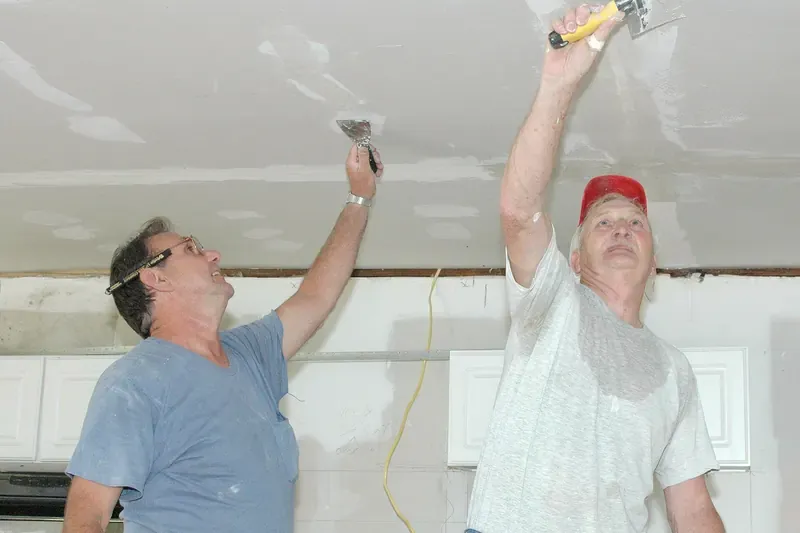 Two workers scraping damaged ceiling drywall after a flood